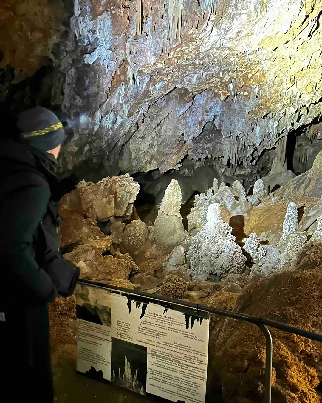 visiteur devant les choux-fleurs de cristaux dans la grotte avec le panneau